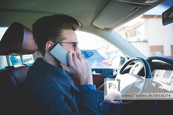 Stylish young man talking on smartphone whilst driving car