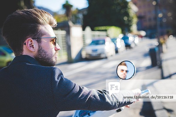Stilvoller junger Mann schaut vom Moped weg