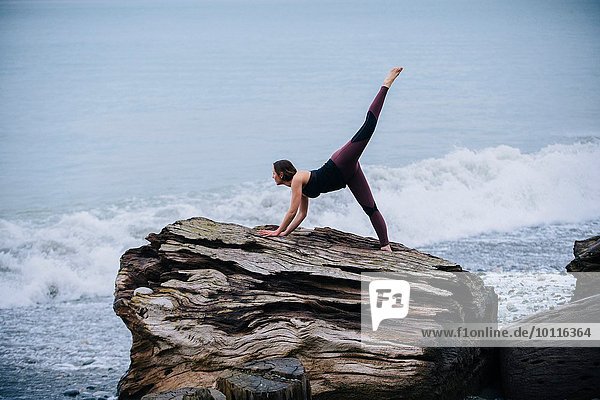 Reife Frau beim Yoga am großen Treibholzbaumstumpf am Strand