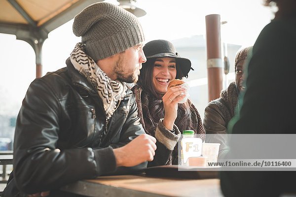 Vier junge erwachsene Freunde beim Plaudern und Donuts essen im Straßencafé