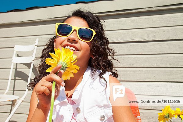Porträt eines Mädchens mit gelber Sonnenbrille und Sonnenblume auf der Terrasse