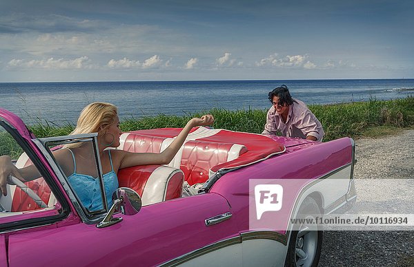 Junger Mann schiebt rosa Vintage Cabrio an der Küste  während Freundin fährt  Havanna  Kuba