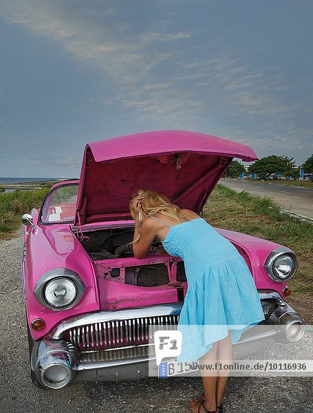Junge Frau versucht  ein Oldtimer Cabriolet an der Küste  Havanna  Kuba zu reparieren.