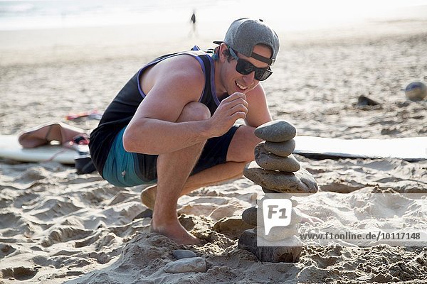 Young man crouching next to a stacked stones on beach
