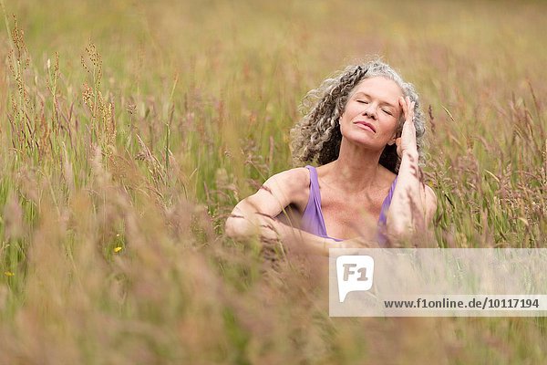 Reife Frau sitzend im langen Gras mit geschlossenen Augen