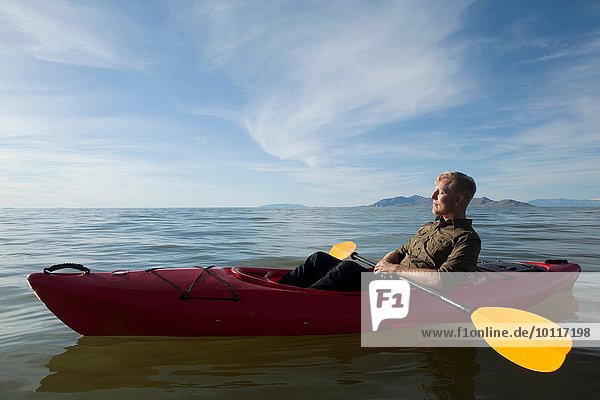 Side view of young man in kayak on water holding paddles  eyes closed  Great Salt Lake  Utah  USA