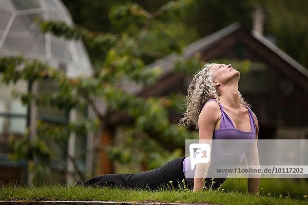 Reife Frau praktiziert Yoga nach oben Hund in Öko-Lodge Garten