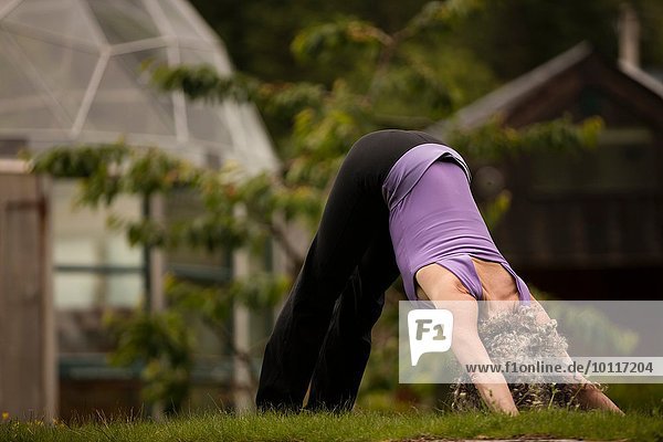 Reife Frau praktiziert Yoga nach unten Hund in Öko-Lodge Garten