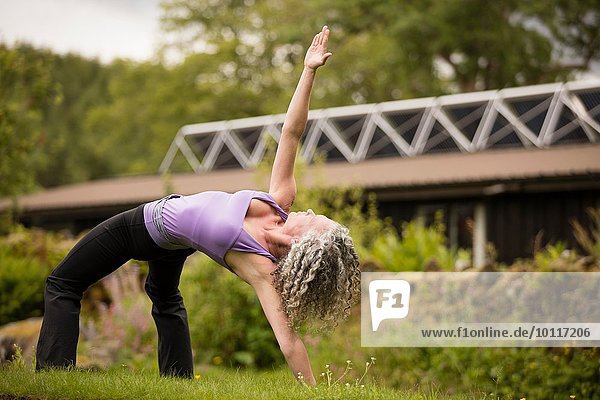 Reife Frau praktiziert Yogabrücke Pose in Öko-Lodge Garten
