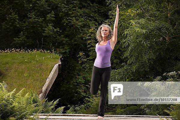 Reife Frau  die Yoga-Pose auf einem Bein im Garten übt