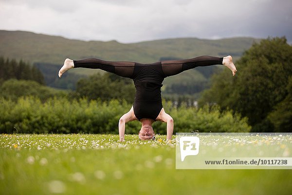 Reife Frau beim Yoga auf dem Kopf stehend mit offenen Beinen im Feld