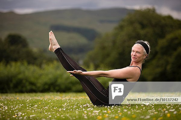 Reife Frau praktiziert Yoga-Boot-Pose im Feld