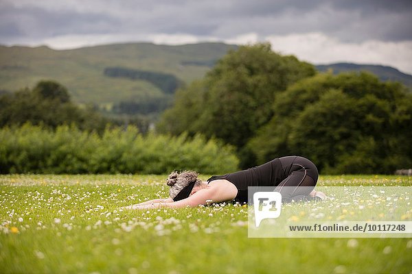 Reife Frau praktiziert Yoga-Kinder Position im Feld