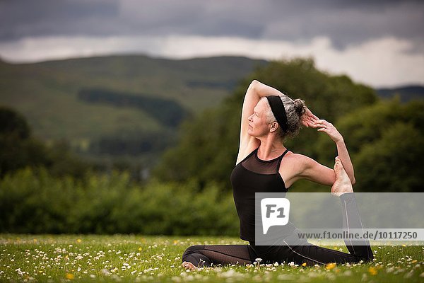 Mature woman doing splits practicing yoga in field