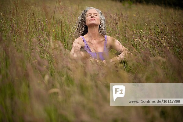 Reife Frau im langen Gras sitzend meditierend