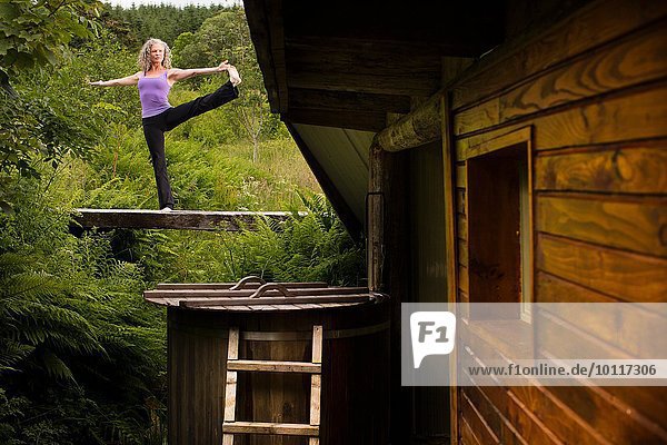 Reife Frau praktiziert Yoga-Pose auf dem Steg in der Öko-Lodge