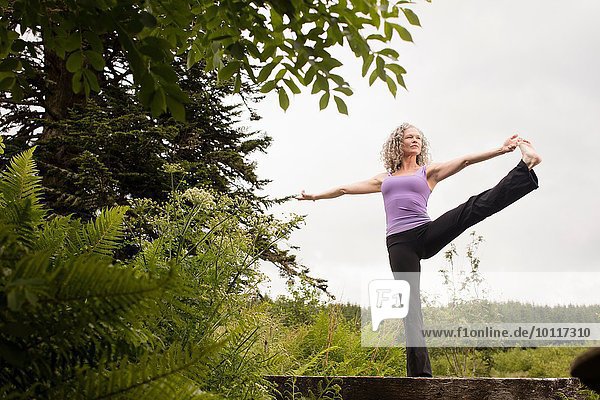 Reife Frau praktiziert Yoga-Pose auf Steg