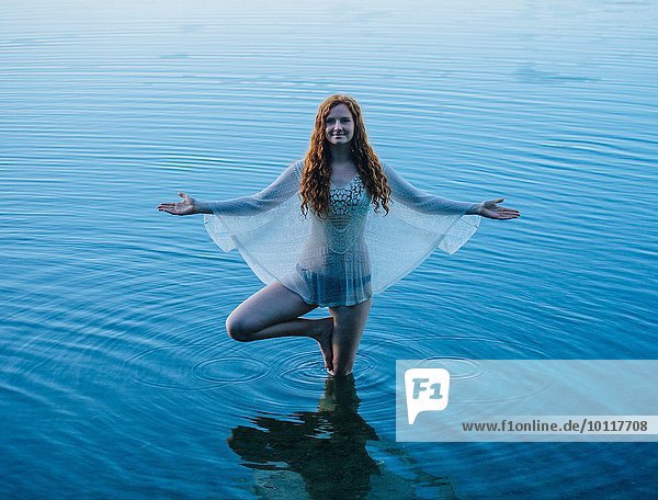 Junge Frau  die im blauen See steht und Yoga praktiziert.
