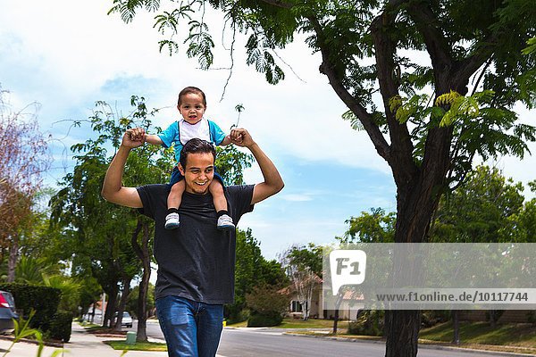 Young man carrying toddler brother on shoulders along suburban sidewalk
