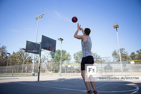 Young male basketball player throwing ball toward basketball hoop
