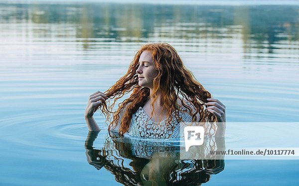 Kopf und Schultern der schönen jungen Frau mit langen roten Haaren im See