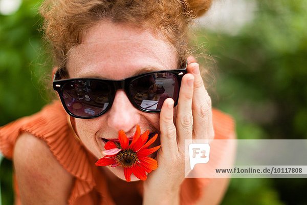 Porträt einer mittelgroßen Frau mit roter Blume im Mund