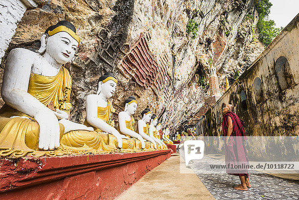 Monk looking at the seated Buddha statues Kawgun Cave Hpa-an Karen or Kayin State Myanmar Asia