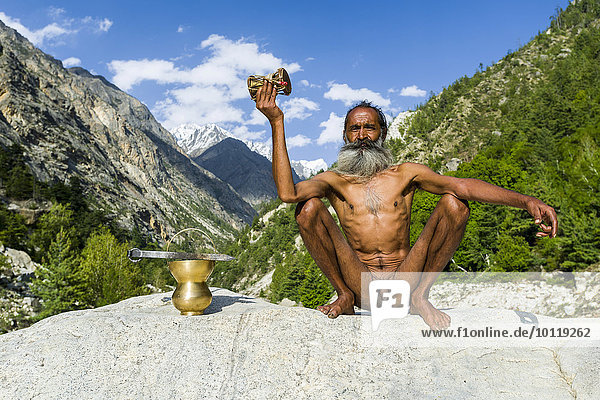Mahant Naomi Giri  52 Jahre  Sadhu  im Lotussitz  padmasana  auf einem Felsen am Ufer des heiligen Flusses Ganges  betend mit seiner Trommel  Gangotri  Uttarakhand  Indien  Asien
