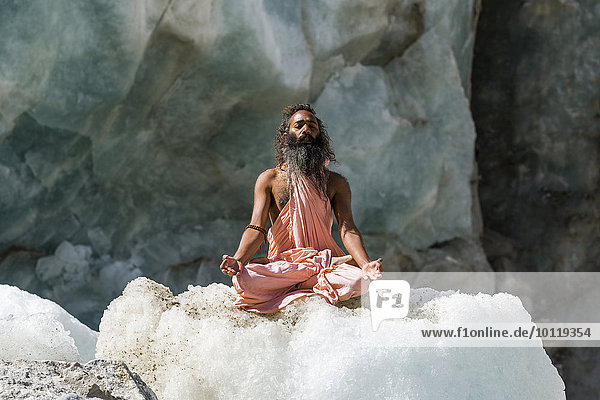 Ein Sadhu  heiliger Mann  meditierend im Lotussitz  padmasana  auf einem Eisblock am Gaumukh  Hauptquelle des Ganges  Gangotri  Uttarakhand  Indien  Asien