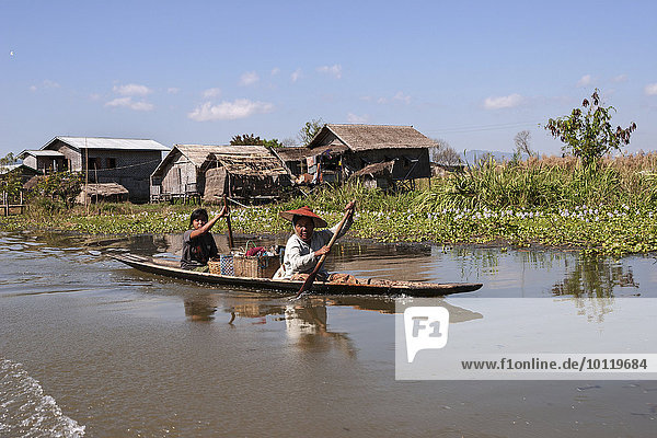 Traditionelle Stelzenhäuser im Inle-See  vorne zwei einheimische Frauen in einem Holzboot  Shan-Staat  Myanmar  Asien