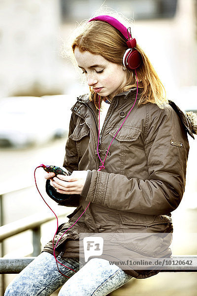 Girl  red-head  with smartphone and headphones in the city