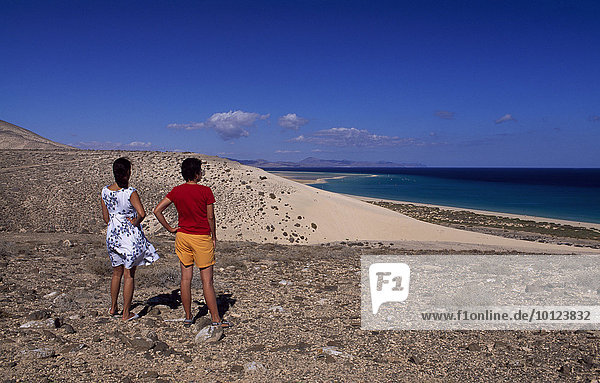 Zwei Menschen  Rückenansicht  mit Blick auf die Küste bei Sotavento  Fuerteventura  Kanarische Inseln  Spanien  Europa