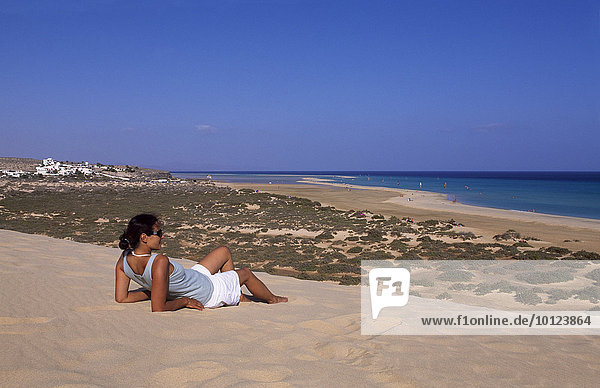 Woman lying on a sand dune overlooking the Playas de Sotavento Beach on Fuerteventura  Canary Islands  Spain  Europe
