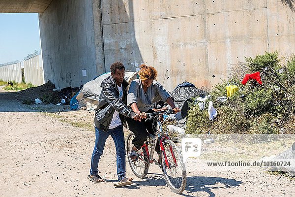 The Jungle  Calais  France. Eritrean illegal immigrant or migrant  teaching a fellow refugee how to ride a bike  just outside the refugee camp north of town.