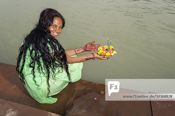 Eine junge Frau mit langen schwarzen Haaren  Henna bemalten Hände und einem grünes Kleid hält ein Deepak  Blumenopfer  an den Ghats des heiligen Flusses Ganges  Rishikesh  Uttarakhand  Indien  Asien