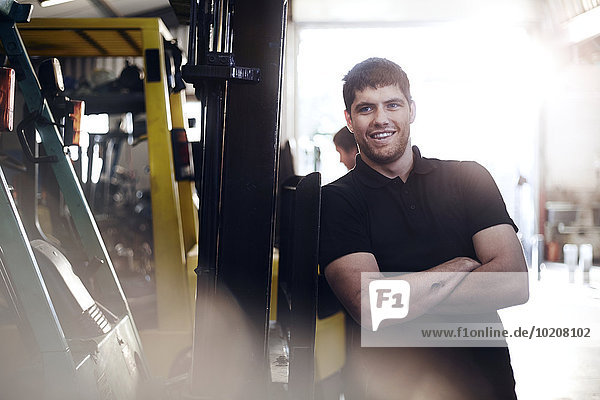 Porträt eines selbstbewussten Mechanikers,  der sich auf einen Gabelstapler in einer Autowerkstatt stützt.