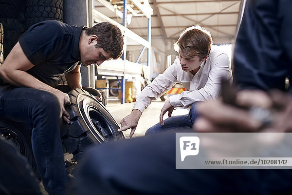 Mechaniker und Kunde prüfen Reifen in der Kfz-Werkstatt