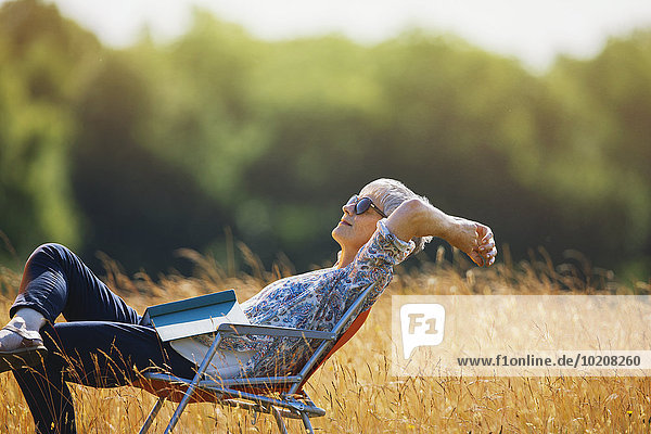 Sorglose Seniorin entspannt mit Buch im sonnigen Feld