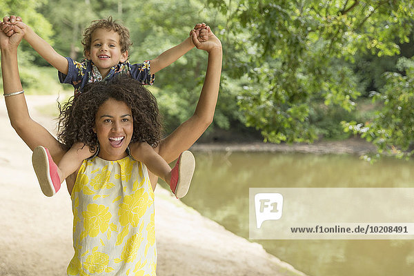 Portrait verspielte Mutter mit Sohn auf Schultern am Teich