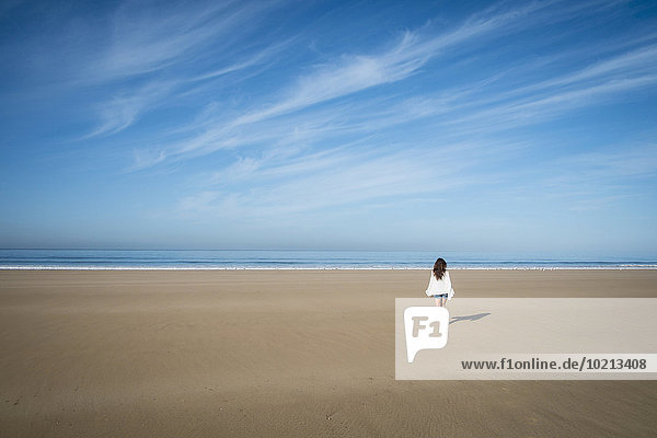 Caucasian woman walking on beach under blue sky