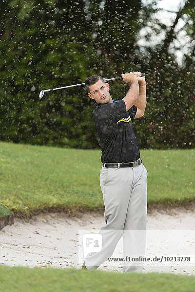 Caucasian man chipping from golf course sand trap