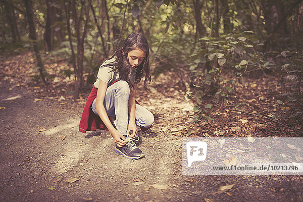 Mixed race girl tying shoelaces on dirt path