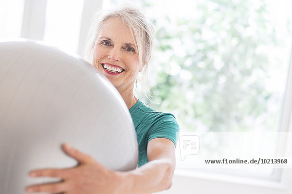 Older Caucasian woman holding exercise ball in gym