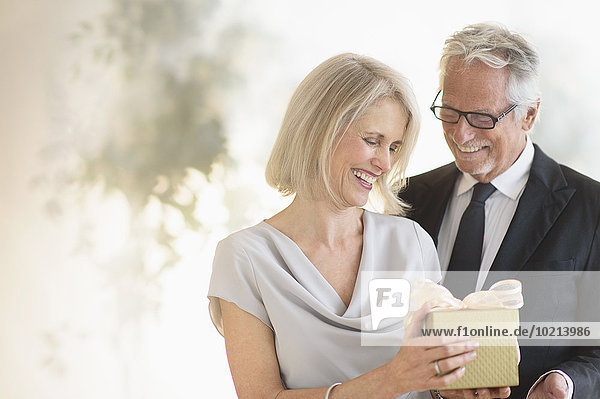 Smiling older Caucasian man giving wife a gift