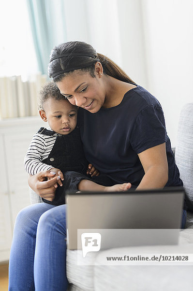 Mixed race mother using laptop with baby son in living room