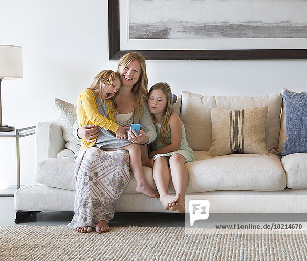 Caucasian mother and daughters using cell phone on sofa