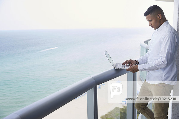 Black businessman using laptop on balcony