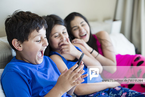 Hispanic siblings using cell phone on sofa