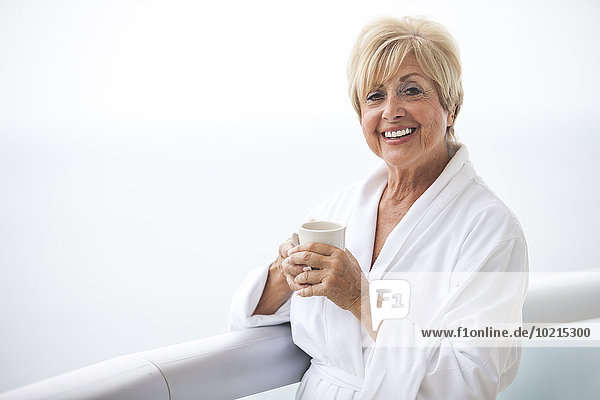 Older Caucasian woman drinking coffee on balcony