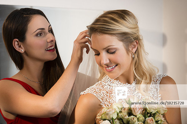 Bridesmaid adjusting veil of bride before wedding